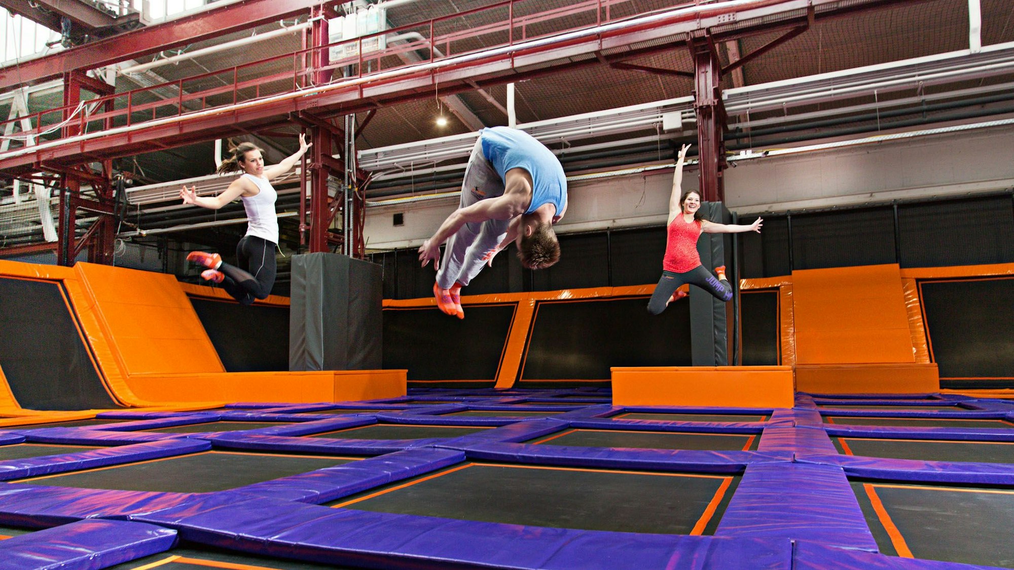 Drei Menschen springen auf Trampolinen im Kölner Jump House. Sie machen unterschiedliche Figuren in der Luft.
