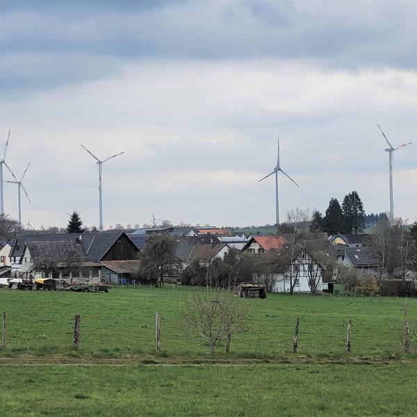 Im Vordergrund ein Dorf, dahinter stehen Windräder.