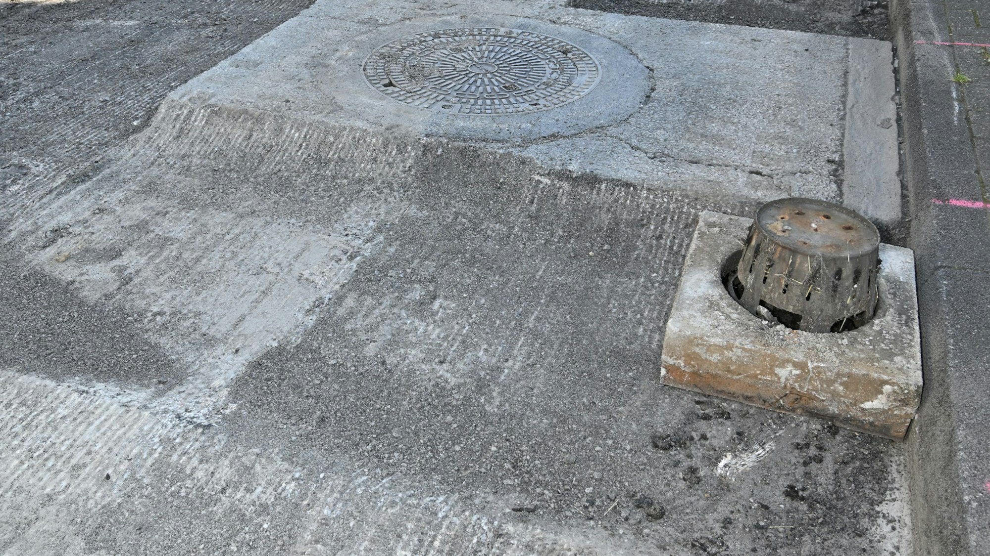 Eine gesperrte Straße ist abgefräst worden, die Kanaldeckel stehen über dem Straßenniveau.