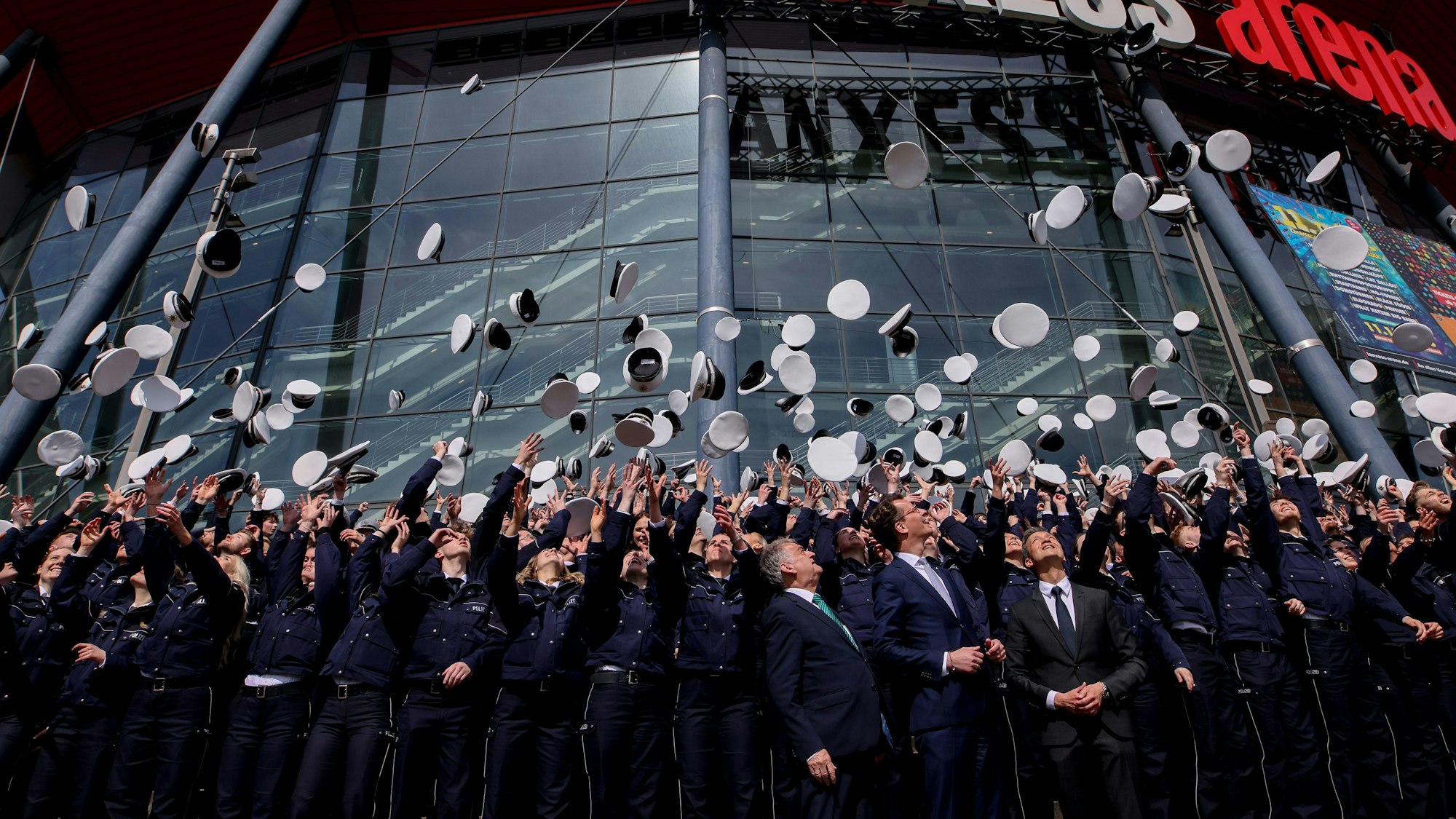 Polizeianwärter werfen ihre Mützen vor der Lanxess Arena in die Luft.
