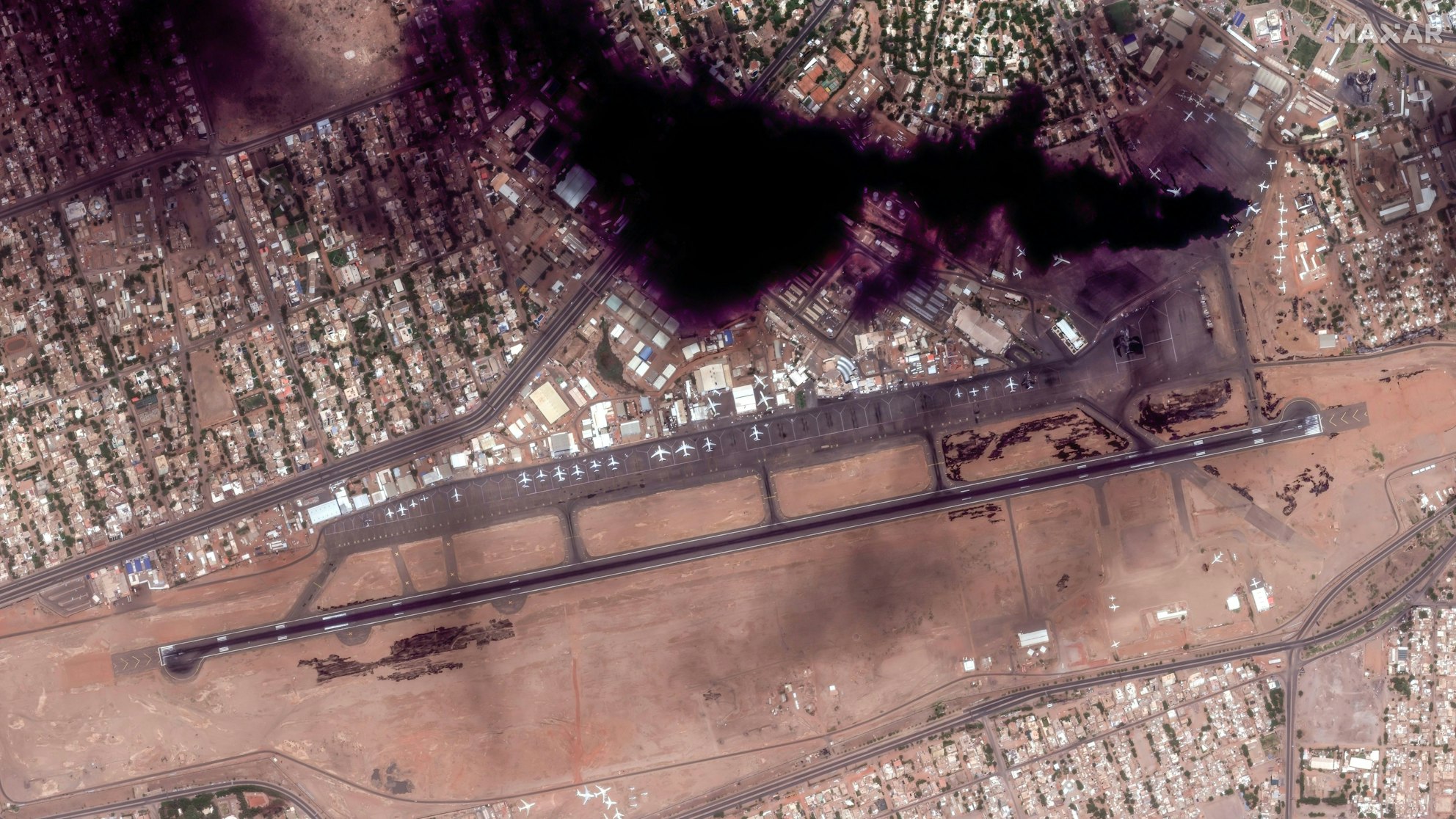 Kämpfe im Sudan: Das Satellitenbild zeigt Rauch und brennende Flugzeuge am Flughafen in Khartum. Die Luftwaffe und andere Nationen wollten am Mittwoch das Rollfeld für Rettungsmissionen nutzen, die wegen anhaltender Kämpfe abgebrochen werden mussten.
