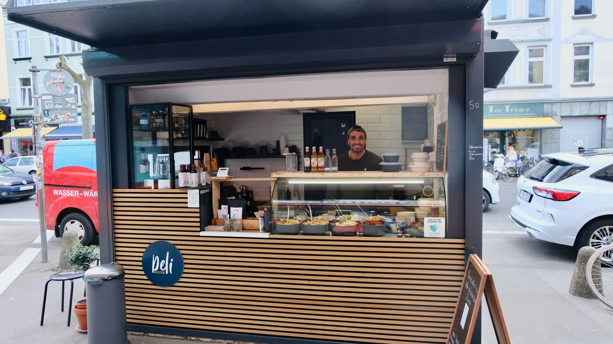 Ein Imbissstand auf einer Straße ist zu sehen. Darin steht ein junger Mann hinter dem Verkaufstresen.