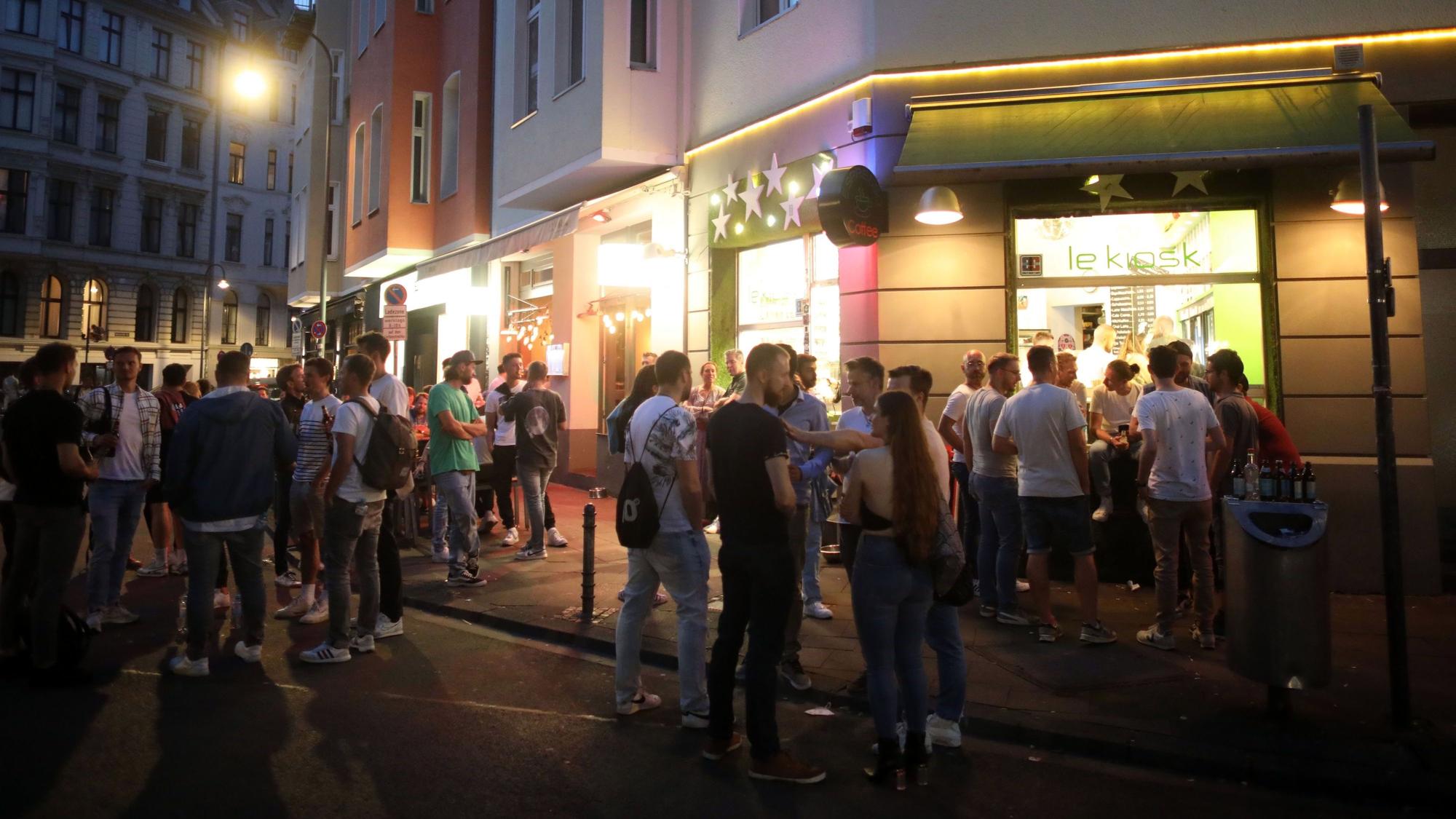 Menschen stehen nachts Schlange an einem Kiosk an der Brüsseler Straße.