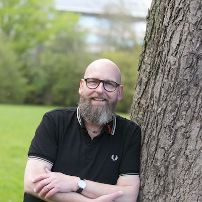 Portrait von Marc Franke. Er lehnt in einem Düsseldorfer Park an einem Baum.