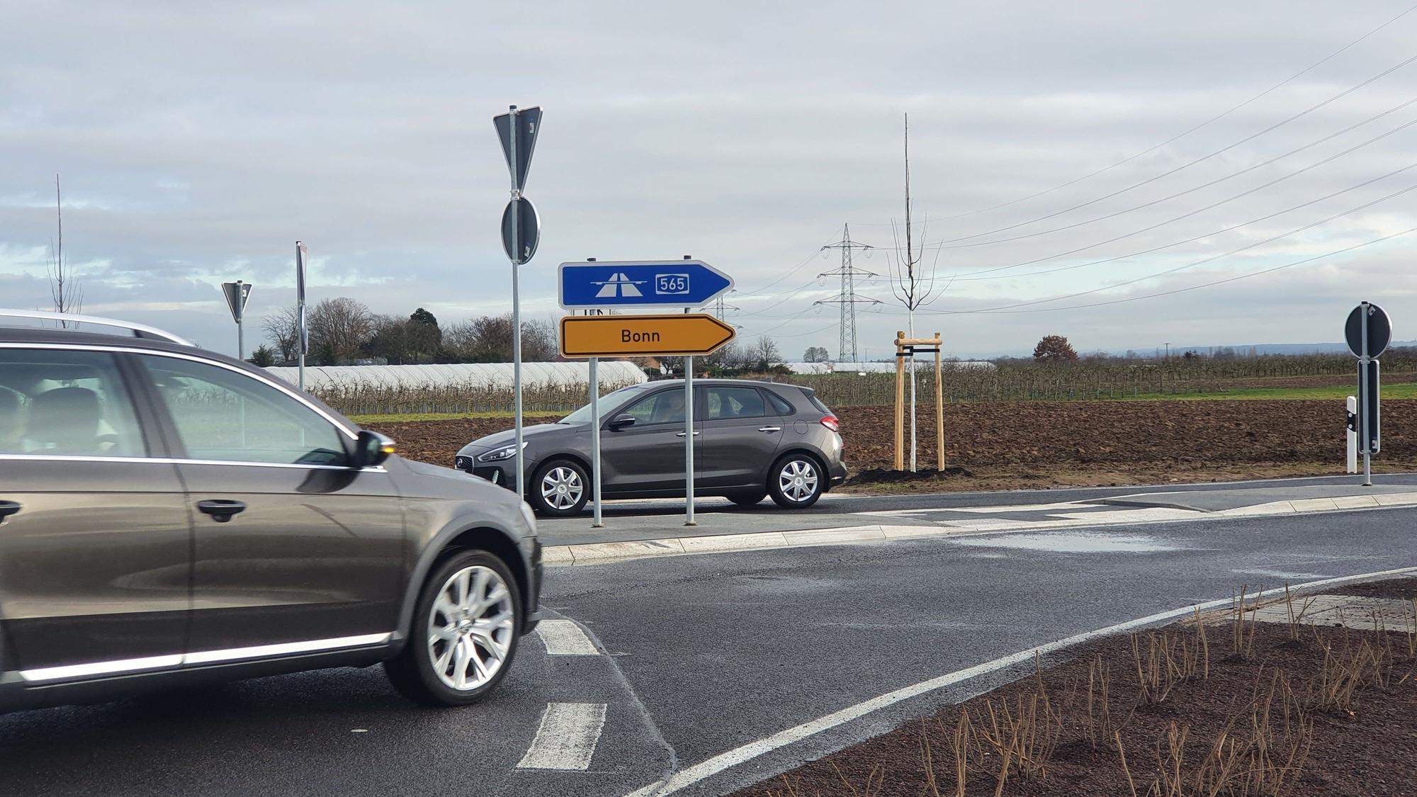 Ein Auto biegt an einem Kreisel ab, Straßenschilder zeigen die Richtungen Bonn und zur Autobahn 565 sn.