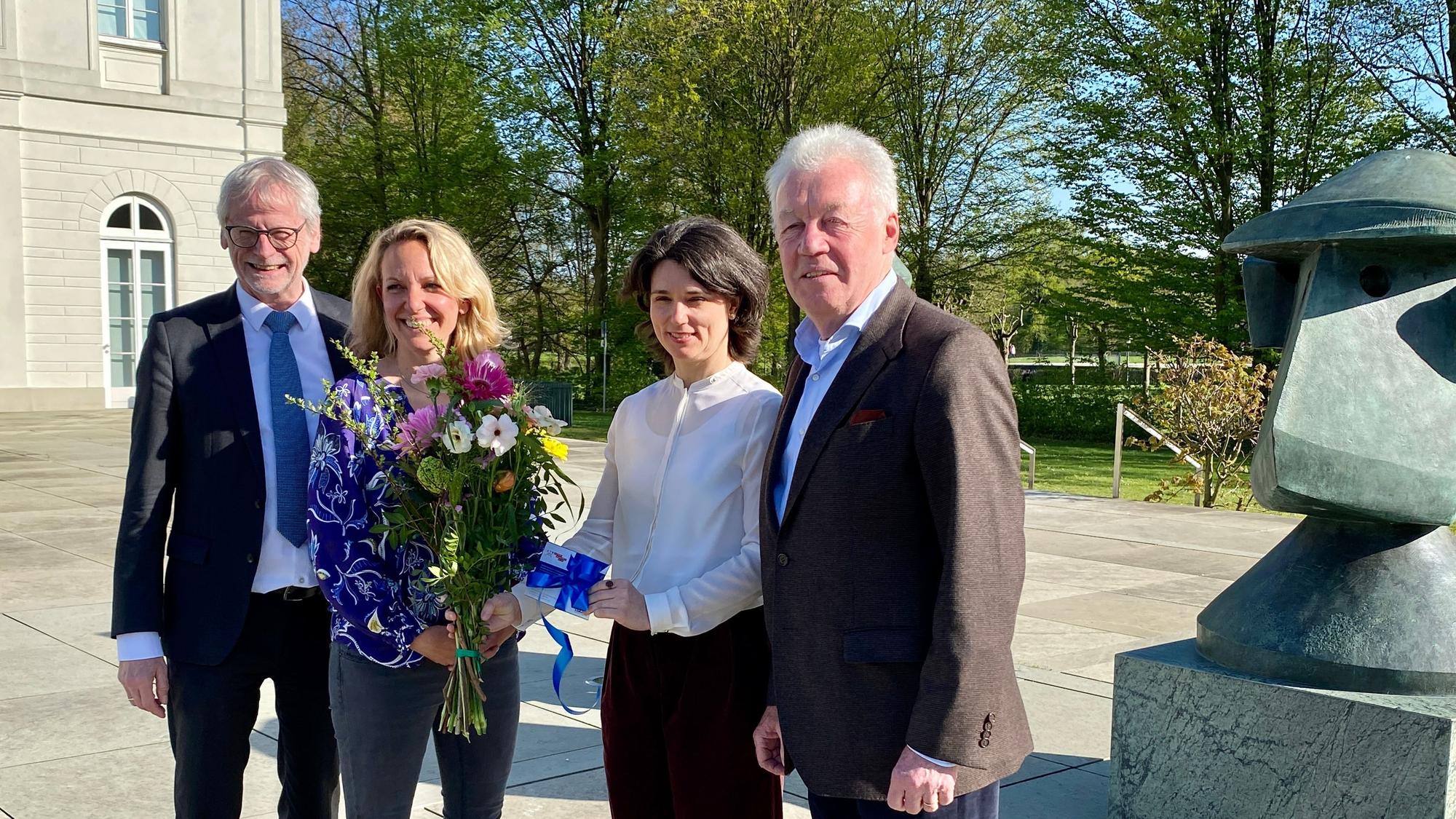 Die Museumsdirektorin überreicht der Kölnerin einen Strauß Blumen und eine Jahreskarte. Beide lächeln in die Kamera. Daneben stehen der Bürgermeister und Vorstandsvorsitzende.