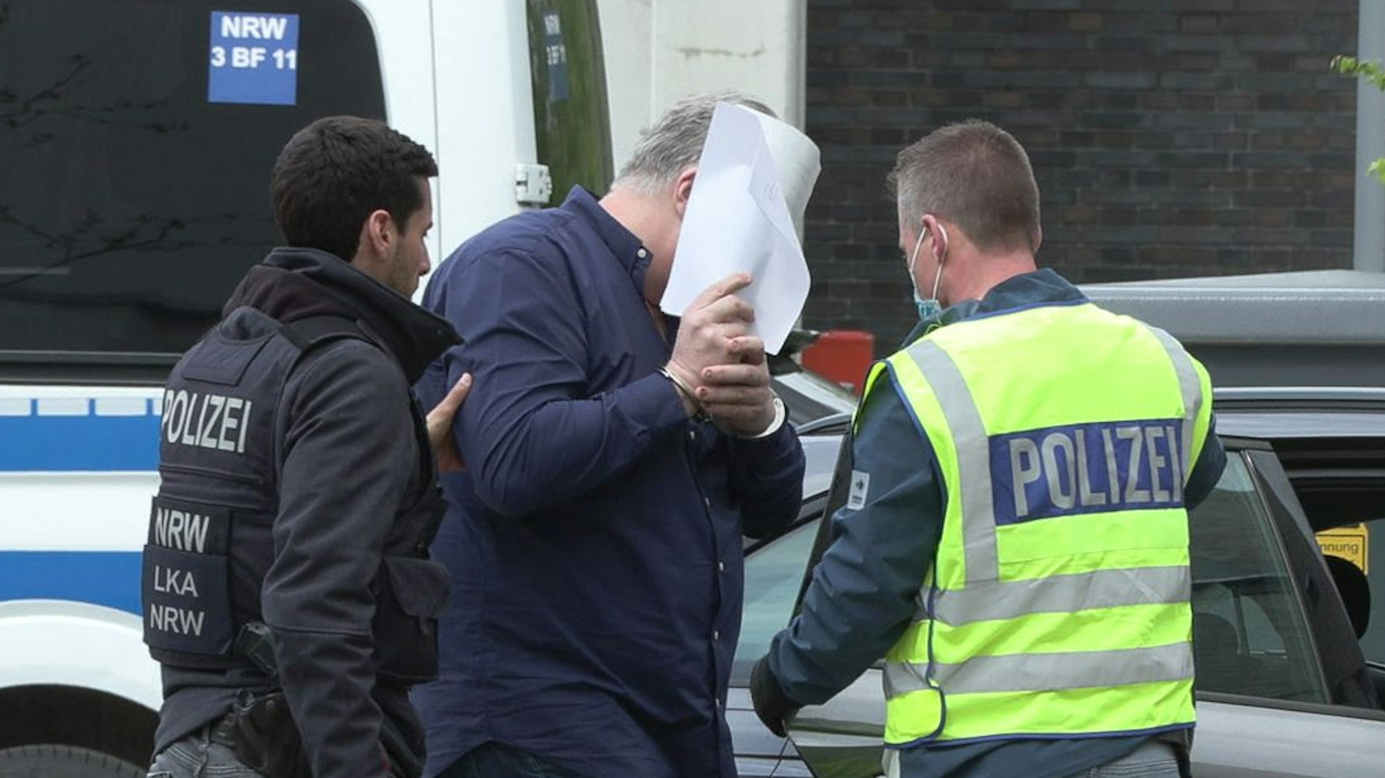 Ein Mann wird von zwei Beamten festgenommen.