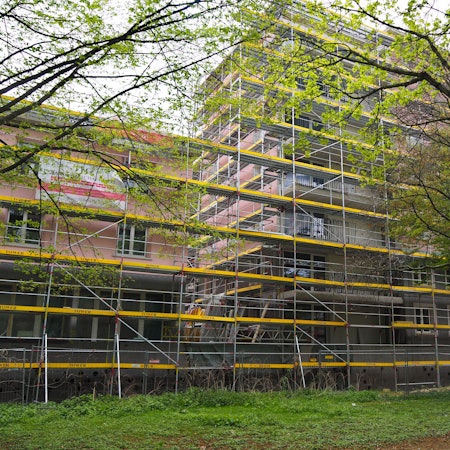 Ein von Baugerüsten umgebenes Gebäude mit rosa Fassade ist zu sehen.