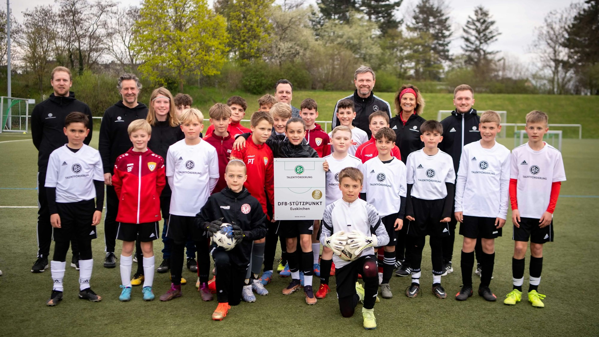 Gemeinsam mit der Plakette posieren alle für ein Foto auf dem Kunstrasenplatz.
