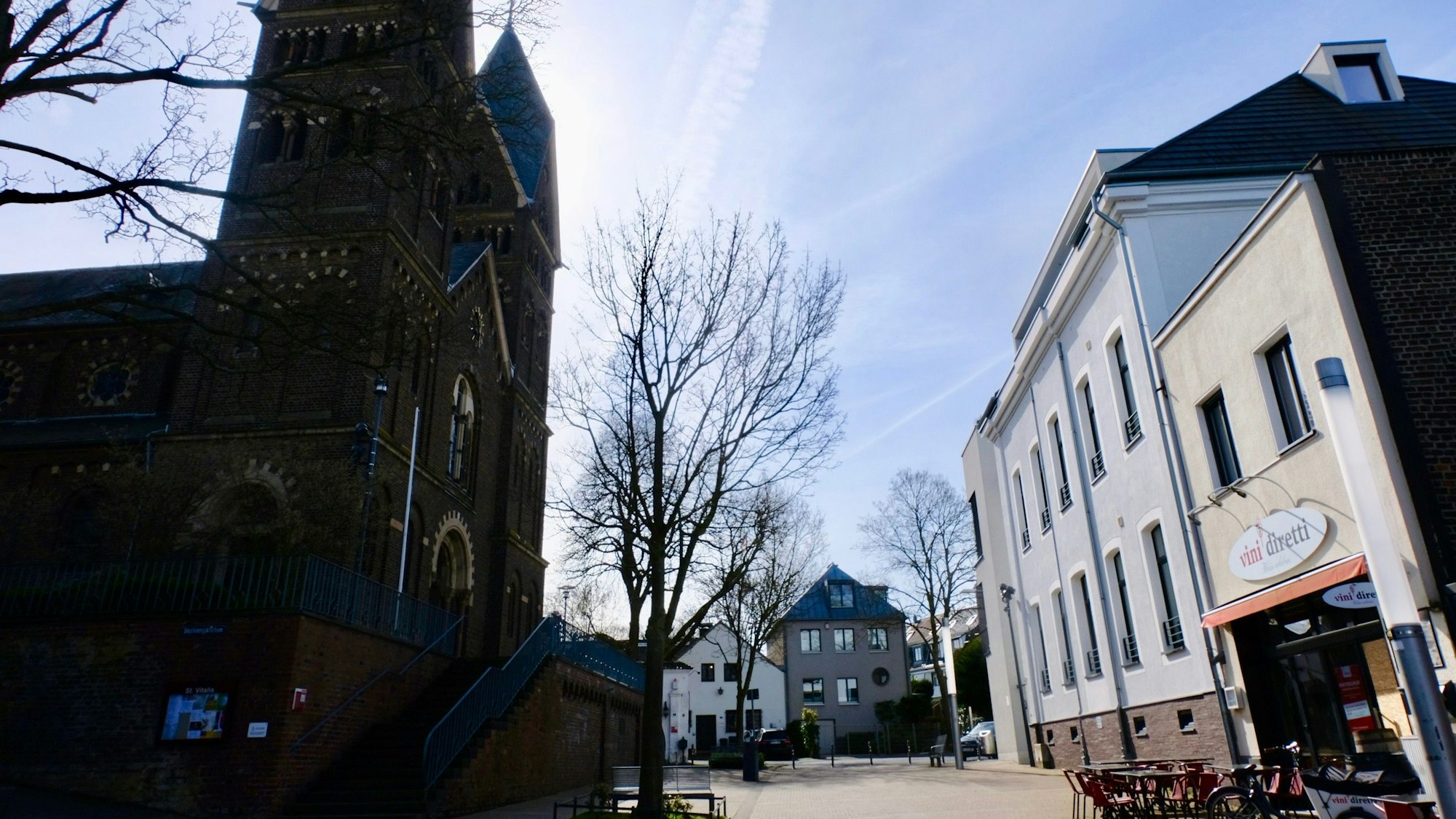 Der Müngersdorfer Dorfplatz mit einer Kirche und Sonnenschein.