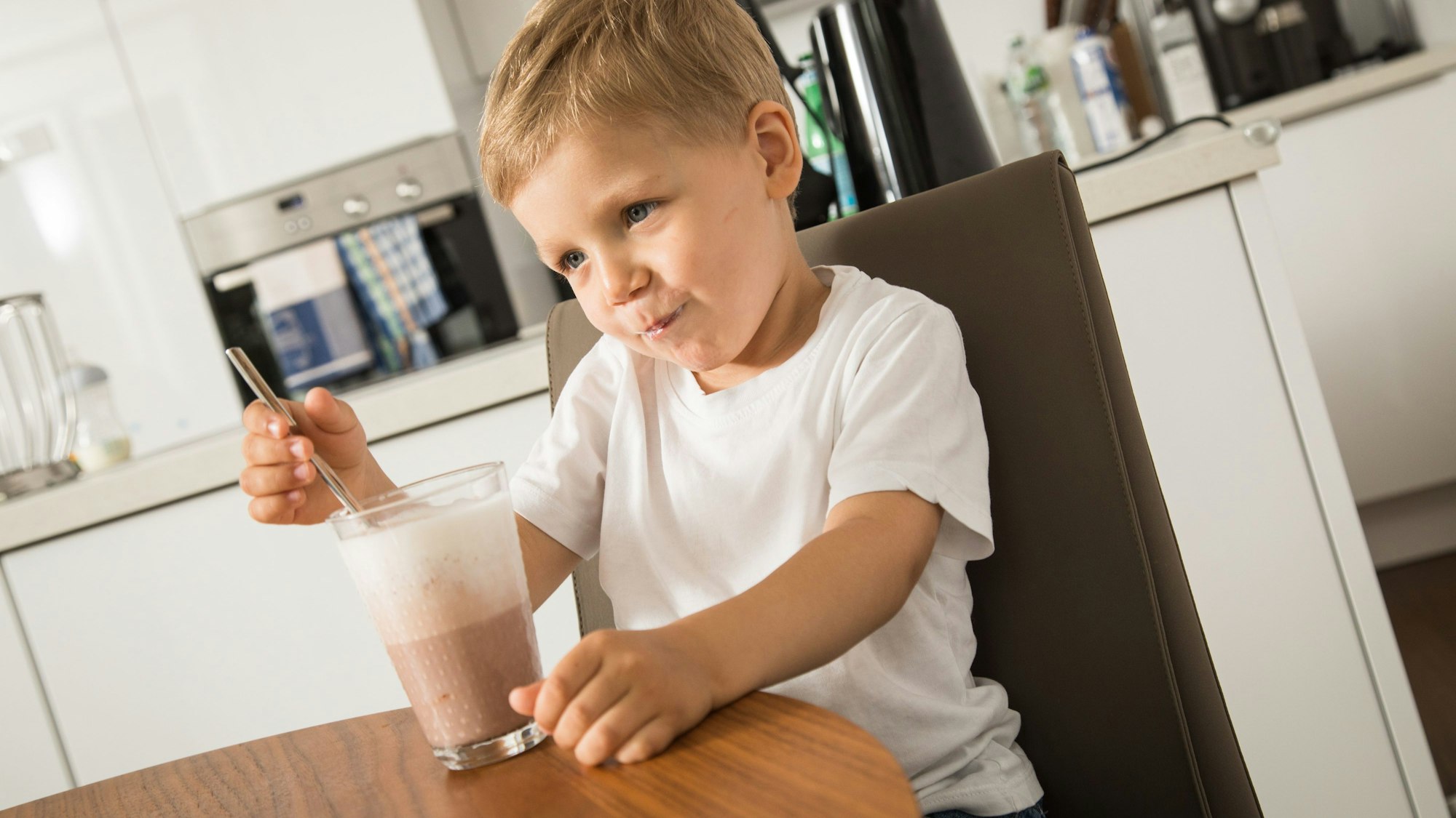 Kleiner Junge mit Kakaoglas am Tisch