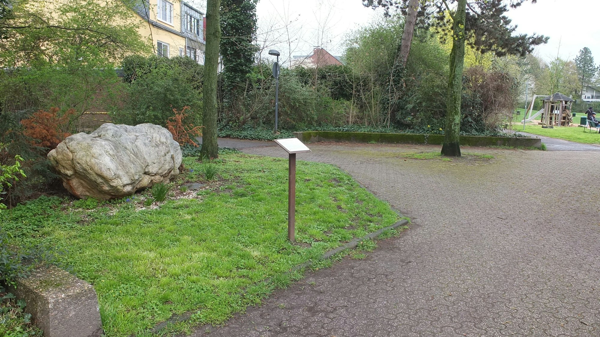 Ein Stein als Denkmal auf einer Wiese mit einem Schild davor.