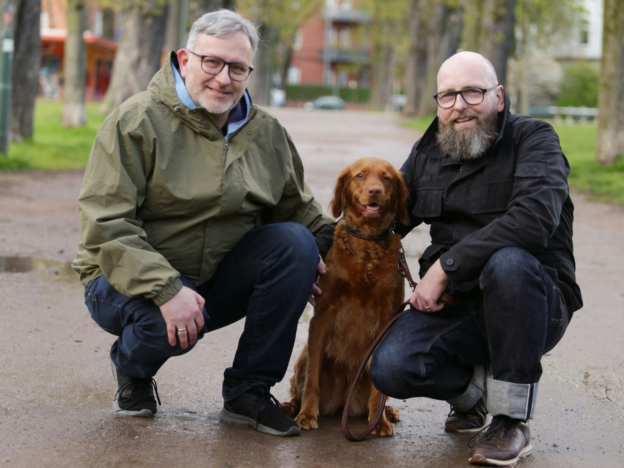 Franke und Sträter gehen in die Hocke, um mit Motte in der mitte für die Kamera zu posieren. Sie sind in einem Park in Düsseldorf.