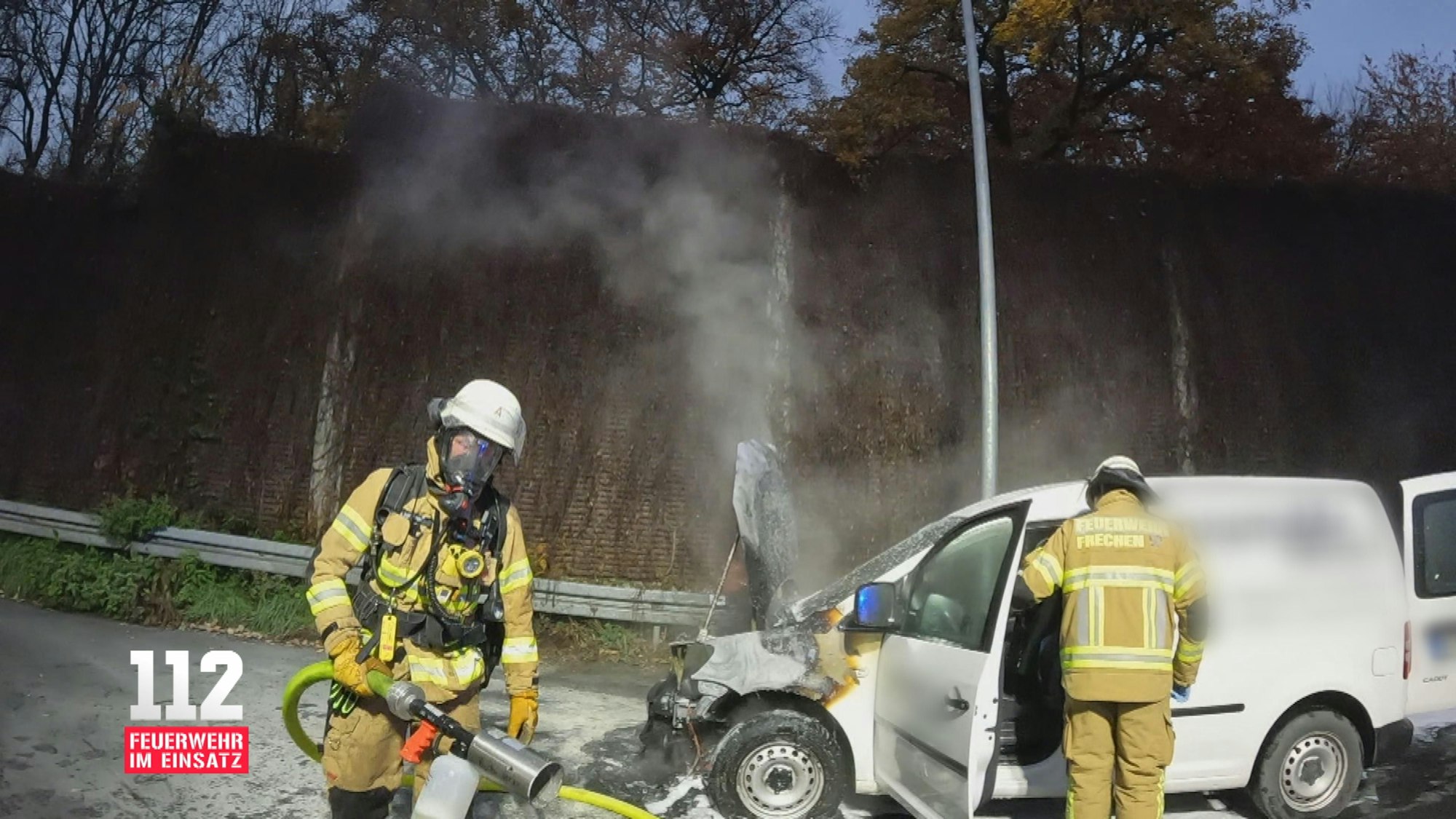 Aufnahme einer Bodycam. Zwei Feuerwehrmänner im Einsatz löschen einen weißen PKW.