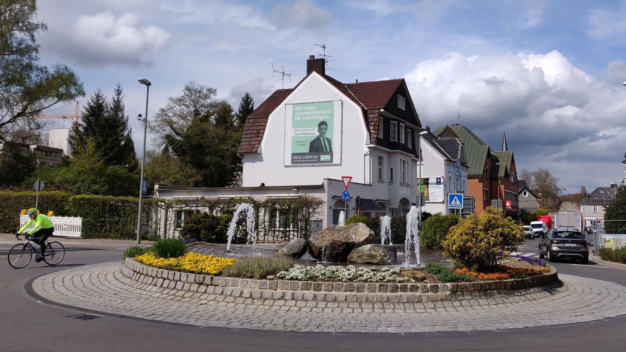 Hauswand mit Werbetafel am Kreisverkehr mit dem Brunnen