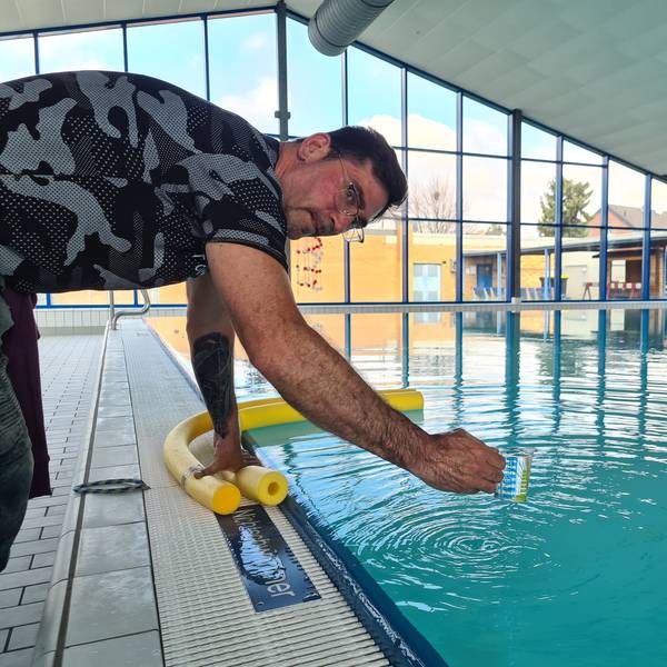 Das Bild zeigt einen Mann, der im Schwimmbad einen Wasserprobe nimmt.