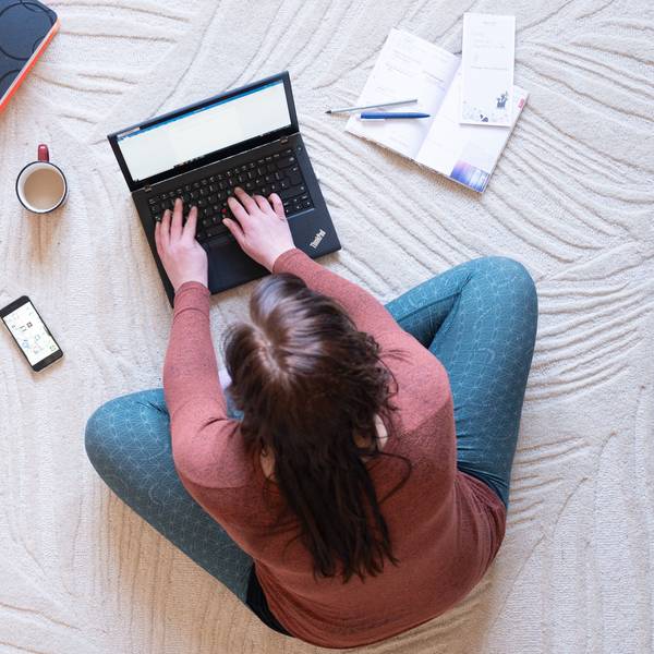Eine Frau sitzt im Homeoffice auf einem Teppich und arbeitet an einem Laptop (Symbolbild).