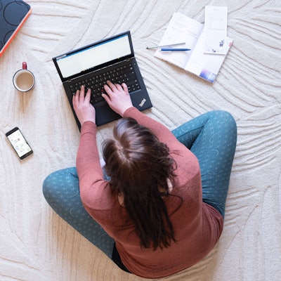Eine Frau sitzt im Homeoffice auf einem Teppich und arbeitet an einem Laptop (Symbolbild).