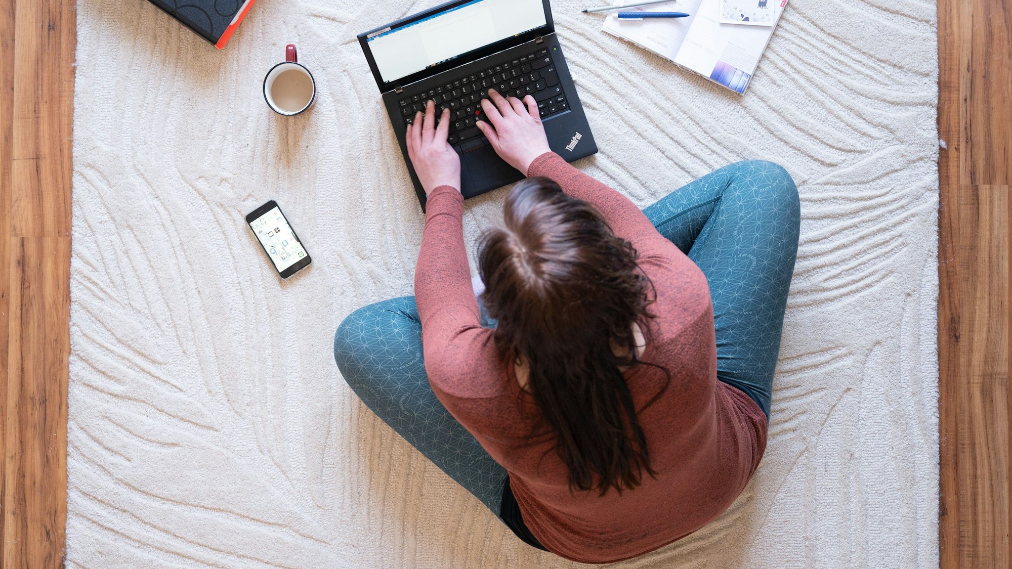 Eine Frau sitzt im Homeoffice auf einem Teppich und arbeitet an einem Laptop (Symbolbild).