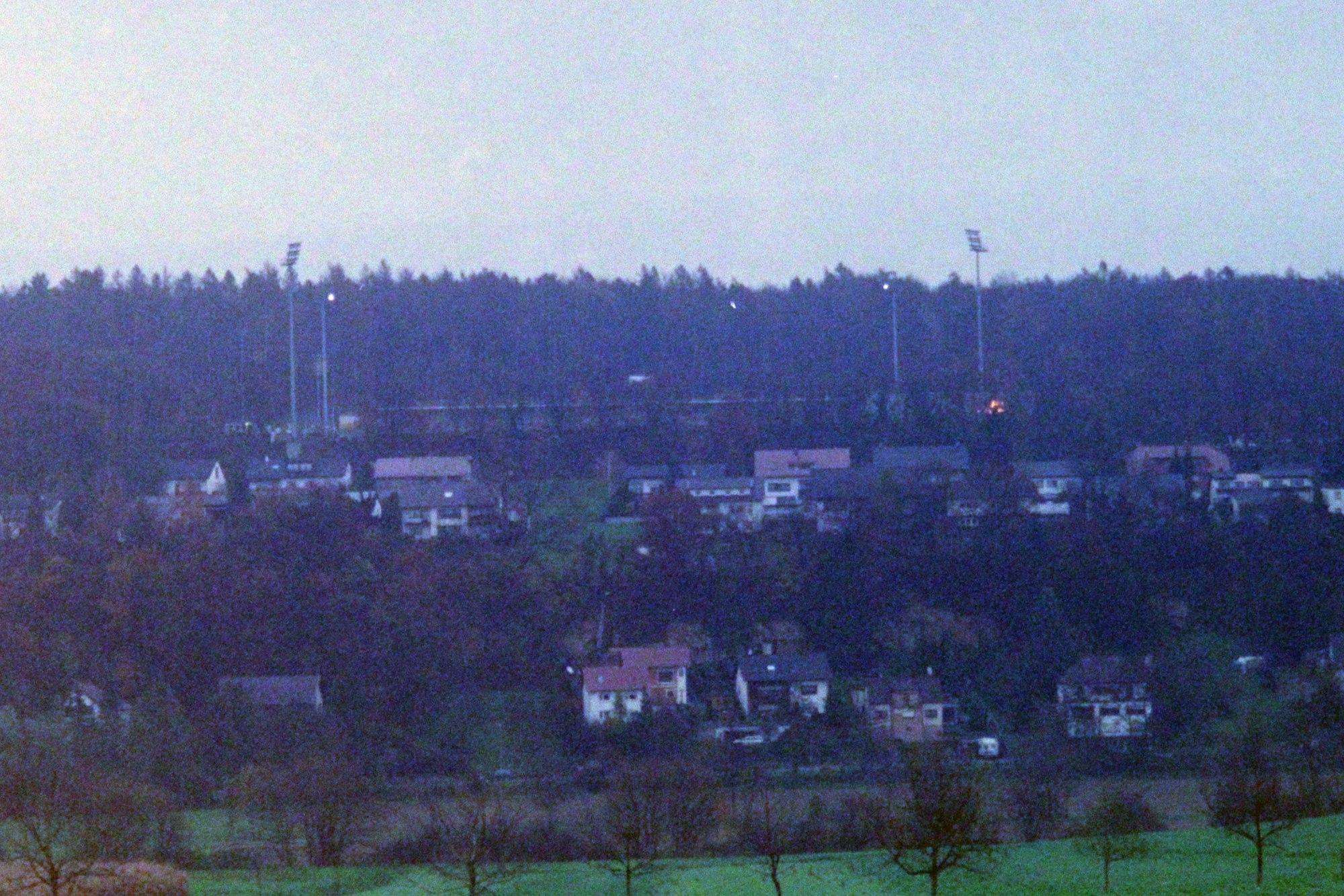 Auf einem Hügel steht ein kleines Fußballstadion vor einem Waldstück.