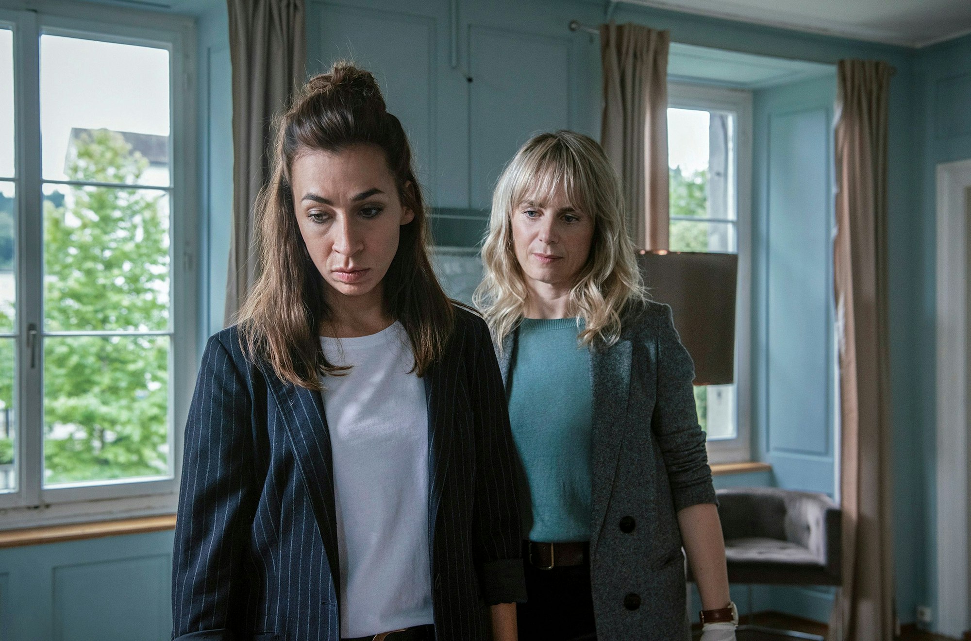 Die Züricher Ermittlerinnen Tessa Ott (Carol Schuler, li.) und Isabelle Grandjean (Anna Pieri Zuercher) stehen in einem Haus, ein Tatort, und blicken beide nach unten.