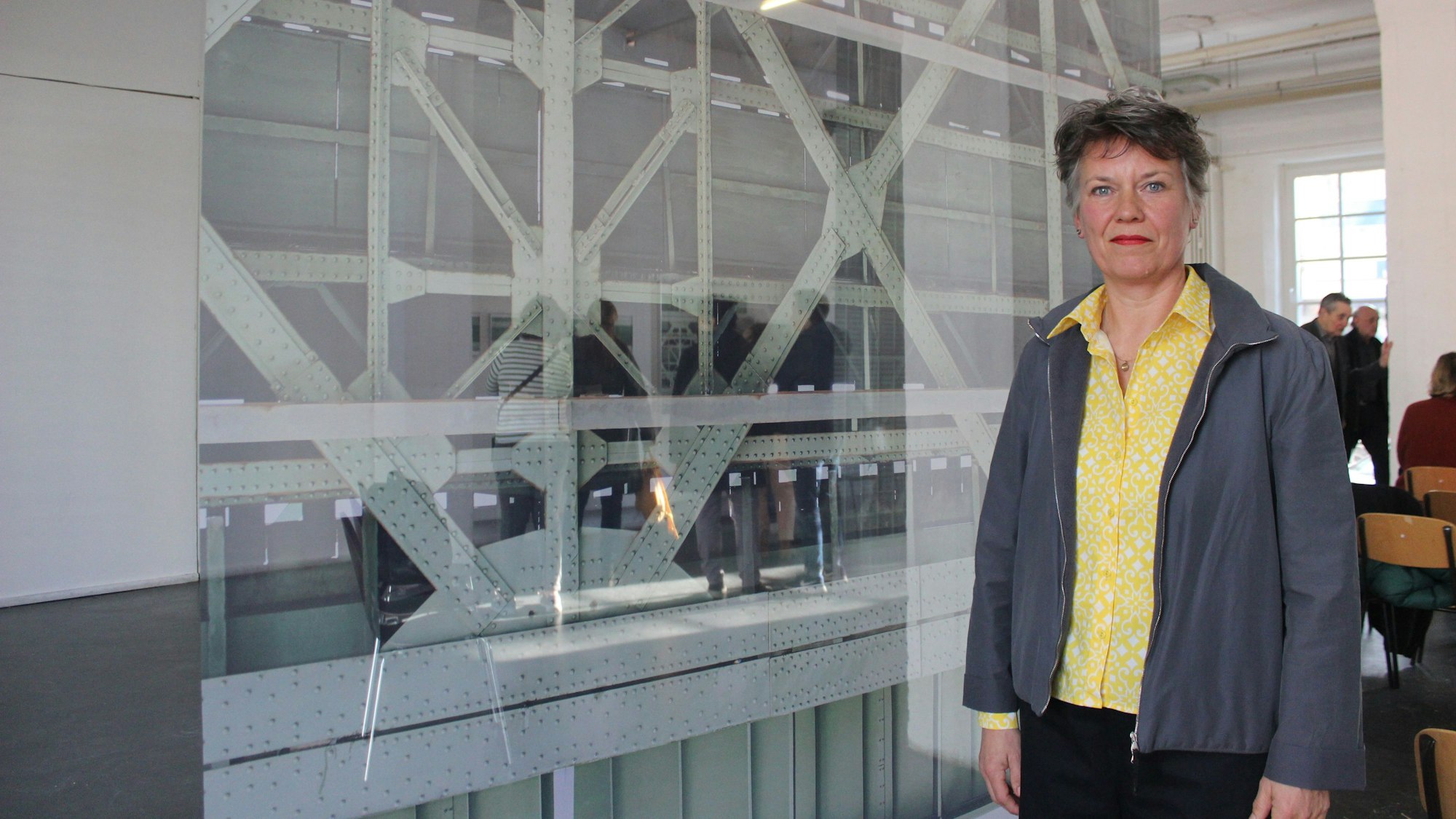 Das Bild zeigt die Künstlerin Anja Schlamann und ein Foto der hell lackierten vernieteten Stahlträger der Südbrücke.