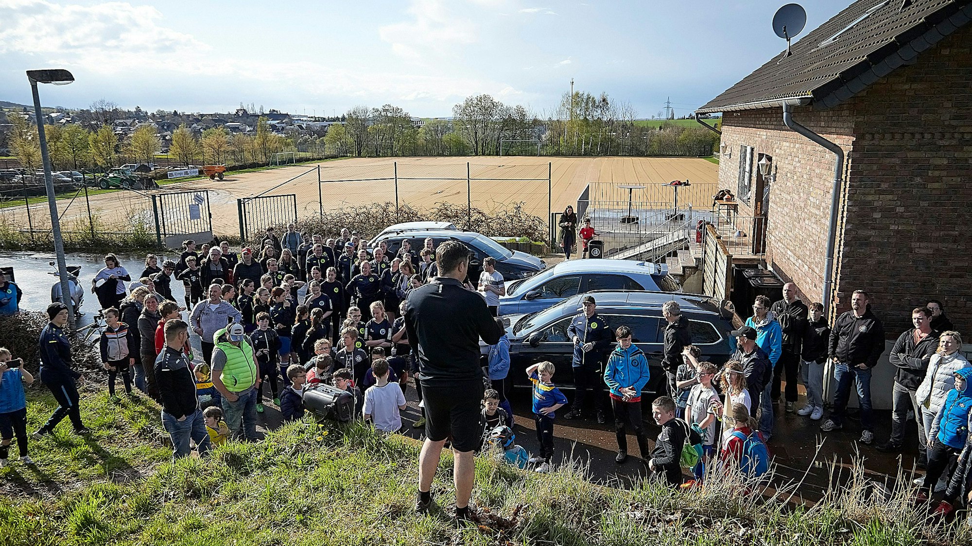 Während rund 100 Vereinsmitglieder einem Vertreter des Vorstands zuhören, sieht man im Hintergrund die Sandfläche des abgetragenen Rasenplatzes.