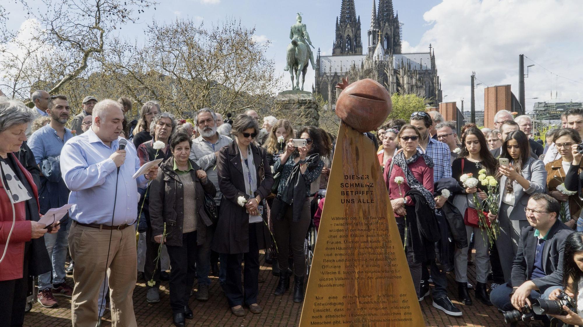 Menschen stehen um die Stele als Denkmal für den Genozid an der armenischen Bevölkerung herum.