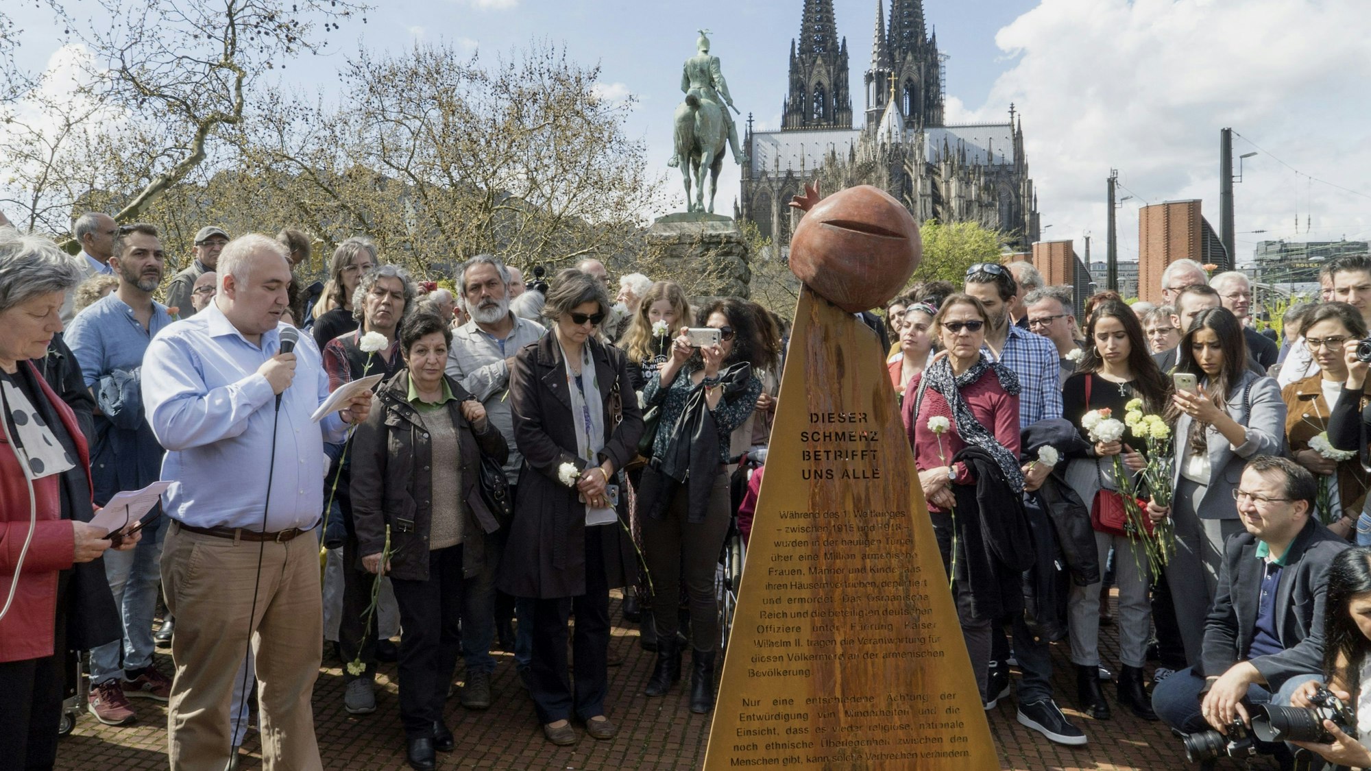 Menschen stehen um die Stele als Denkmal für den Genozid an der armenischen Bevölkerung herum.