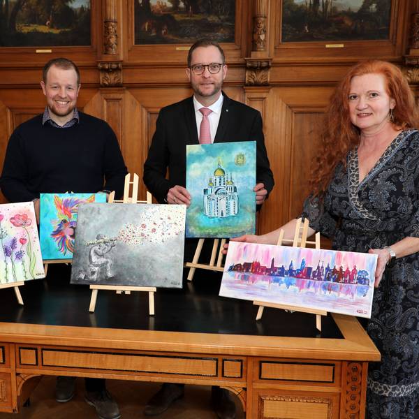 Menschen stehen mit Bildern auf kleinen Staffeleien um einen Tisch im Bergisch Gladbacher Ratssaal.