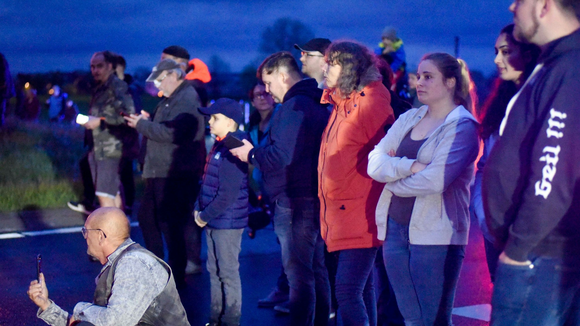 Eine Gruppe von Menschen steht in der Dämmerung neben einer Landstraße.