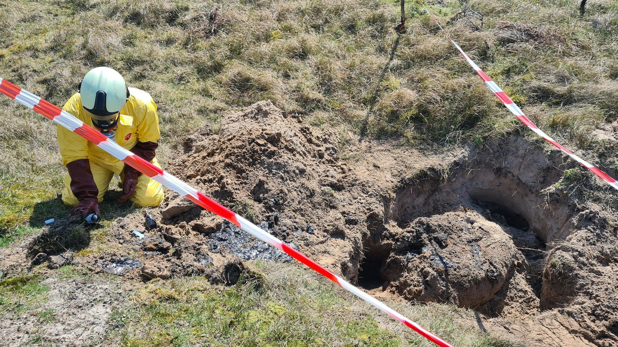 Ein Gefahrgutspezialist der Feuerwehr untersucht in den Dünen im Osten der ostfriesischen Insel Baltrum eine unbekannte, dunkele Substanz. Der Ort ist mit rot-weißem-Flatterband abgesperrt.
