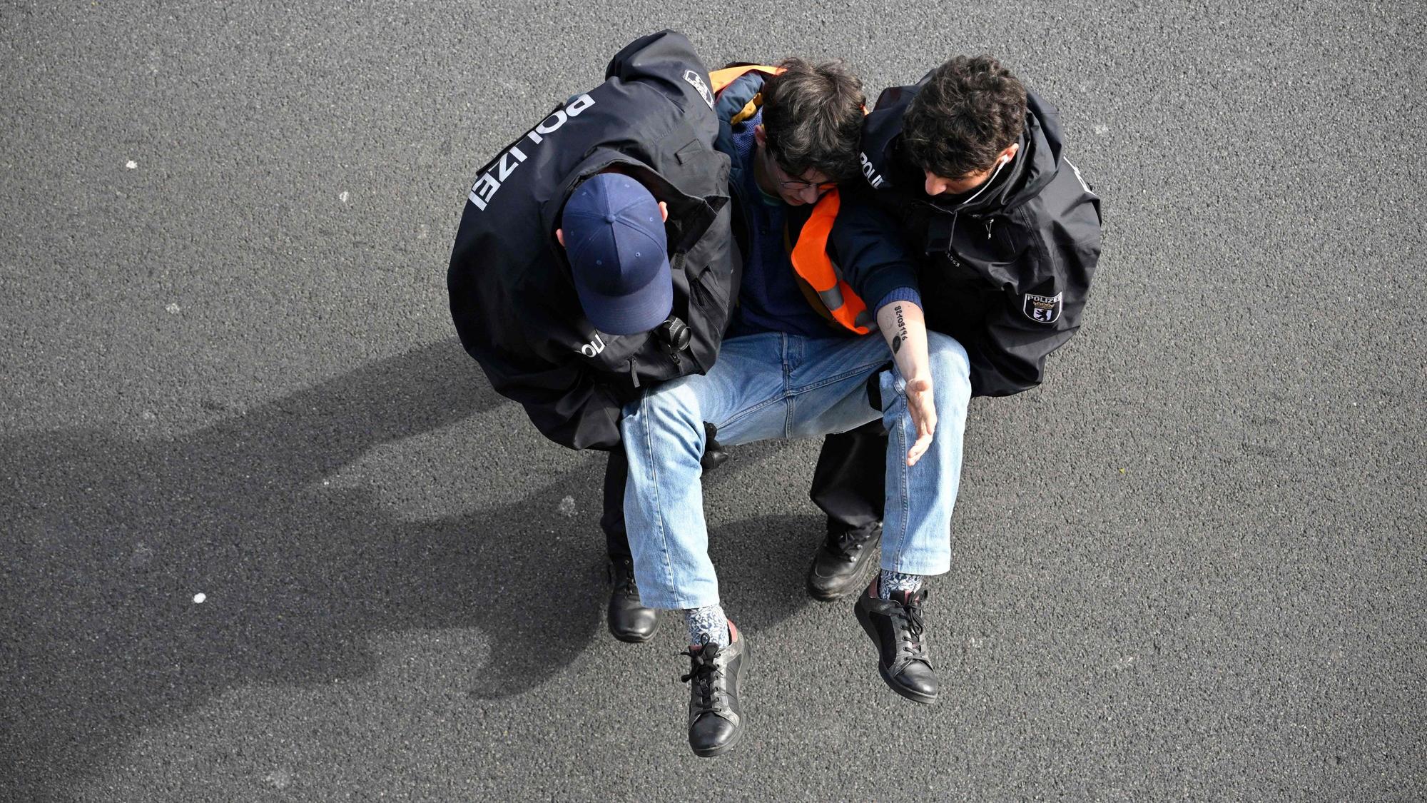 Ein Aktivist wird in Berlin von zwei Polizisten von der Fahrbahn der A100 getragen. Am Montag hat die „Letzte Generation“ nach eigenen Angaben versucht, die Hauptstadt lahmzulegen.