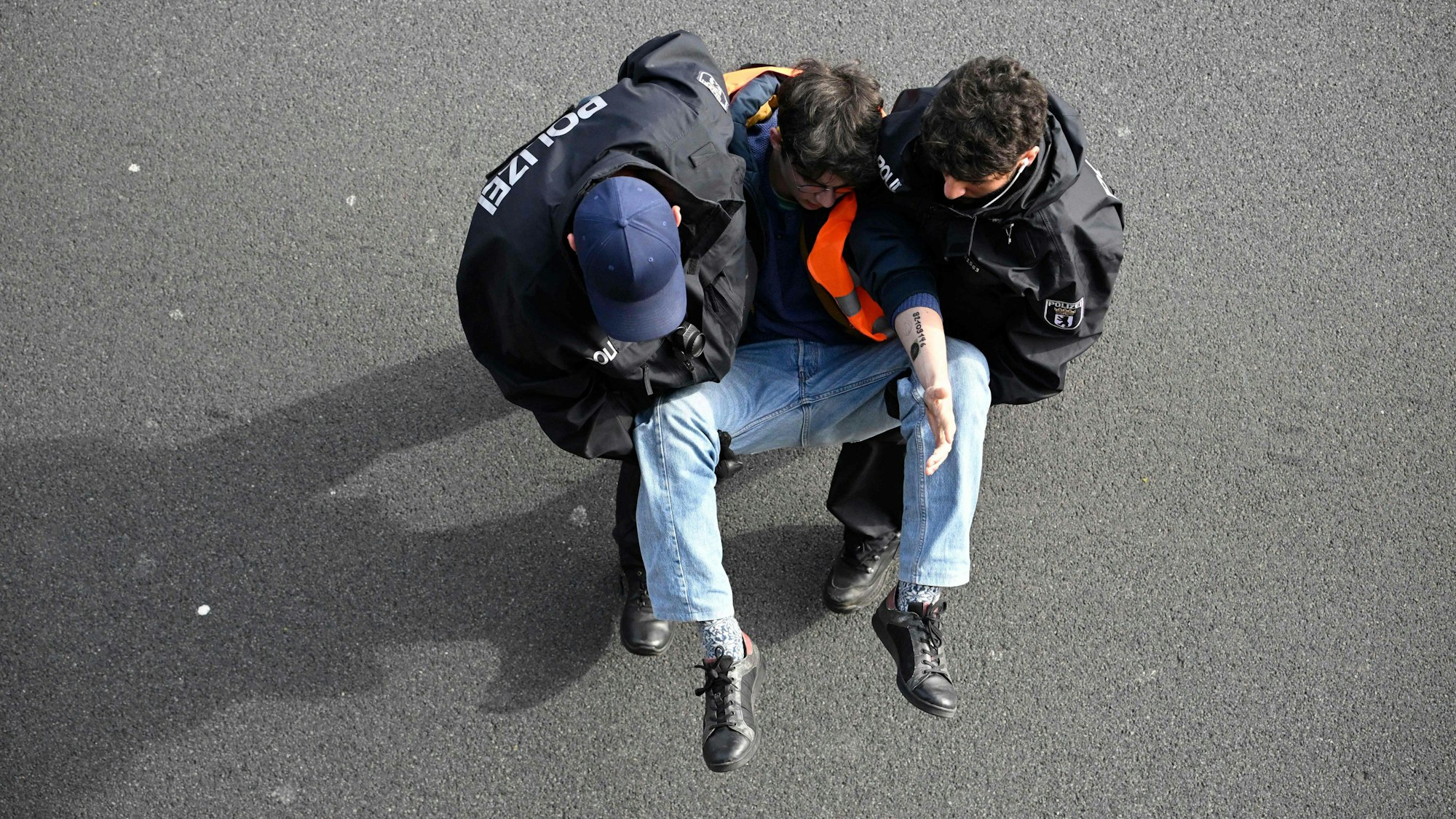Ein Aktivist wird in Berlin von zwei Polizisten von der Fahrbahn der A100 getragen. Am Montag hat die „Letzte Generation“ nach eigenen Angaben versucht, die Hauptstadt lahmzulegen.