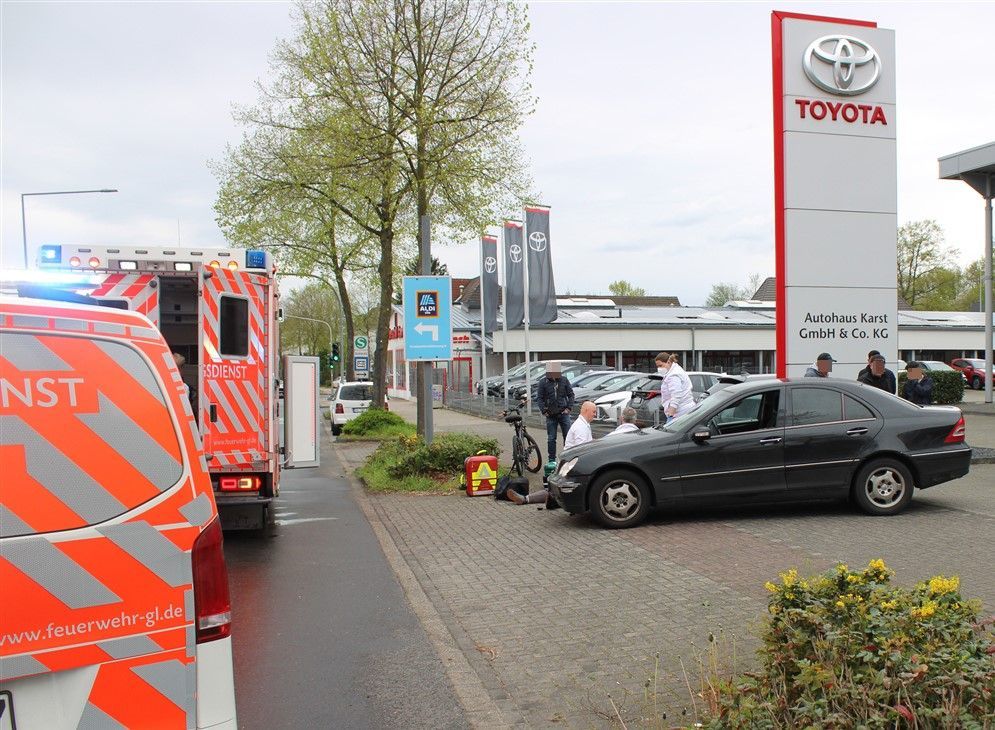Ein Auto steht an der Ausfahrt eines Autohauses. Daneben behandeln Sanitäter eine liegende Person.
