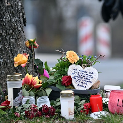 Kerzen und Blumen liegen an einem Baum an der Gesamtschule der getöteten Luise (12) in Freudenberg. Im Hintergrund ist ein Polizist zu sehen.