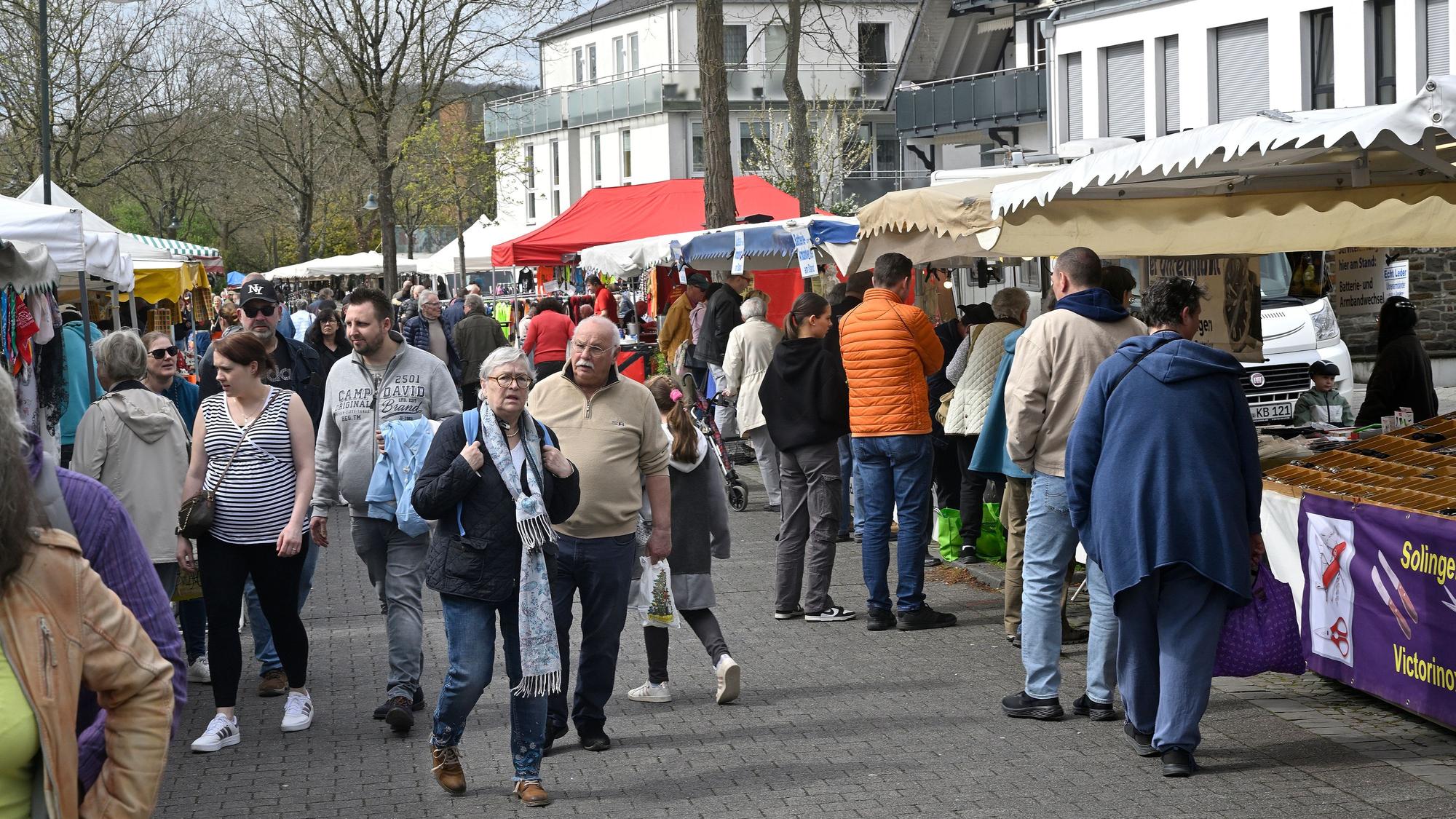 Menschen gehen auf einer Straße zwischen Verkaufsständen und -buden hindurch.