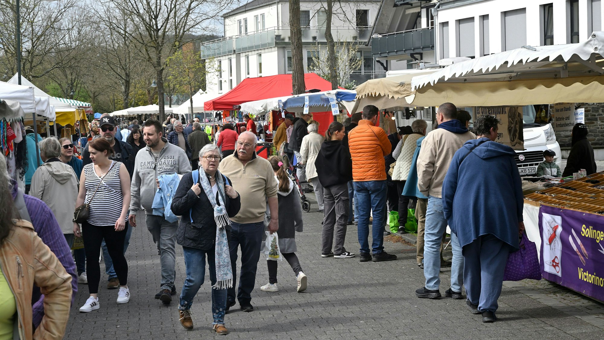 Menschen gehen auf einer Straße zwischen Verkaufsständen und -buden hindurch.