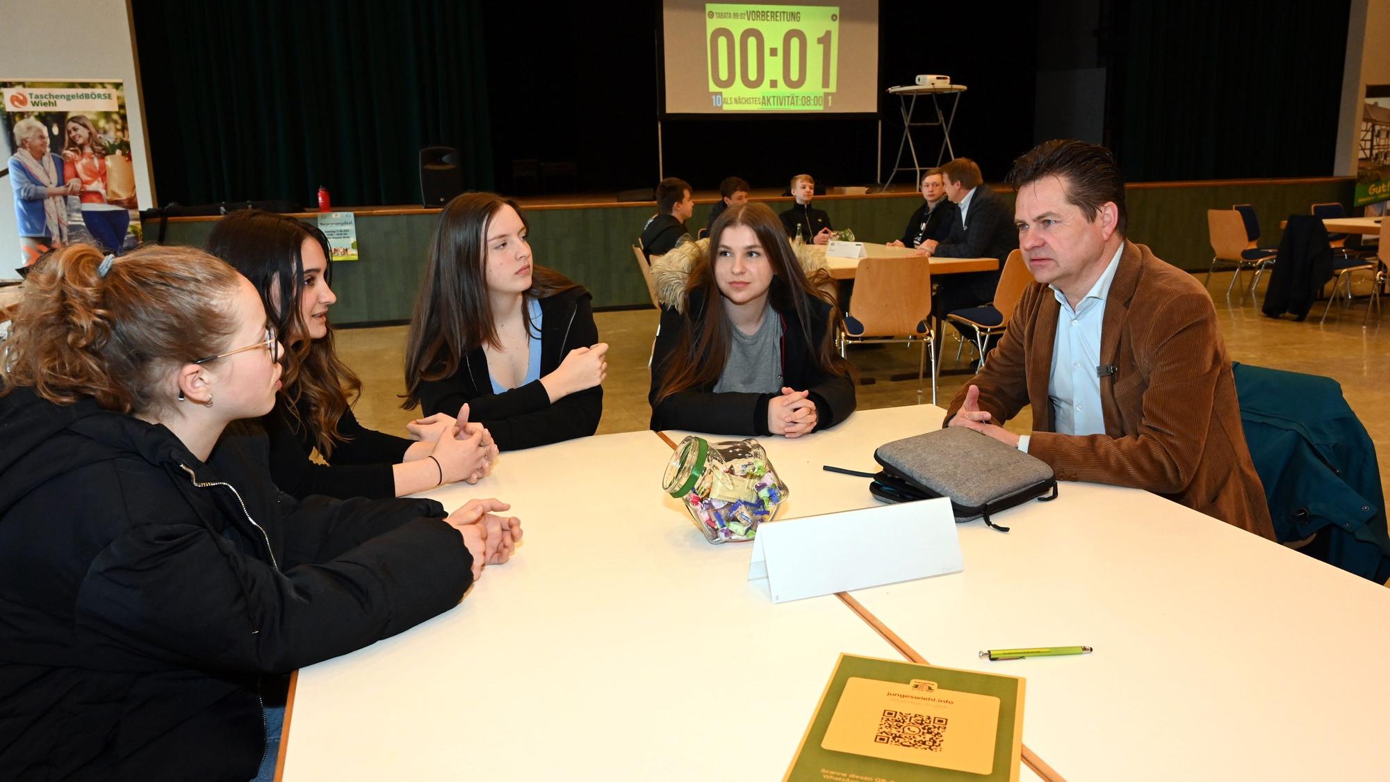 Bürgermeister Ulrich Stücker sitzt an einem Tisch mit vier Neuntklässlerinnen.