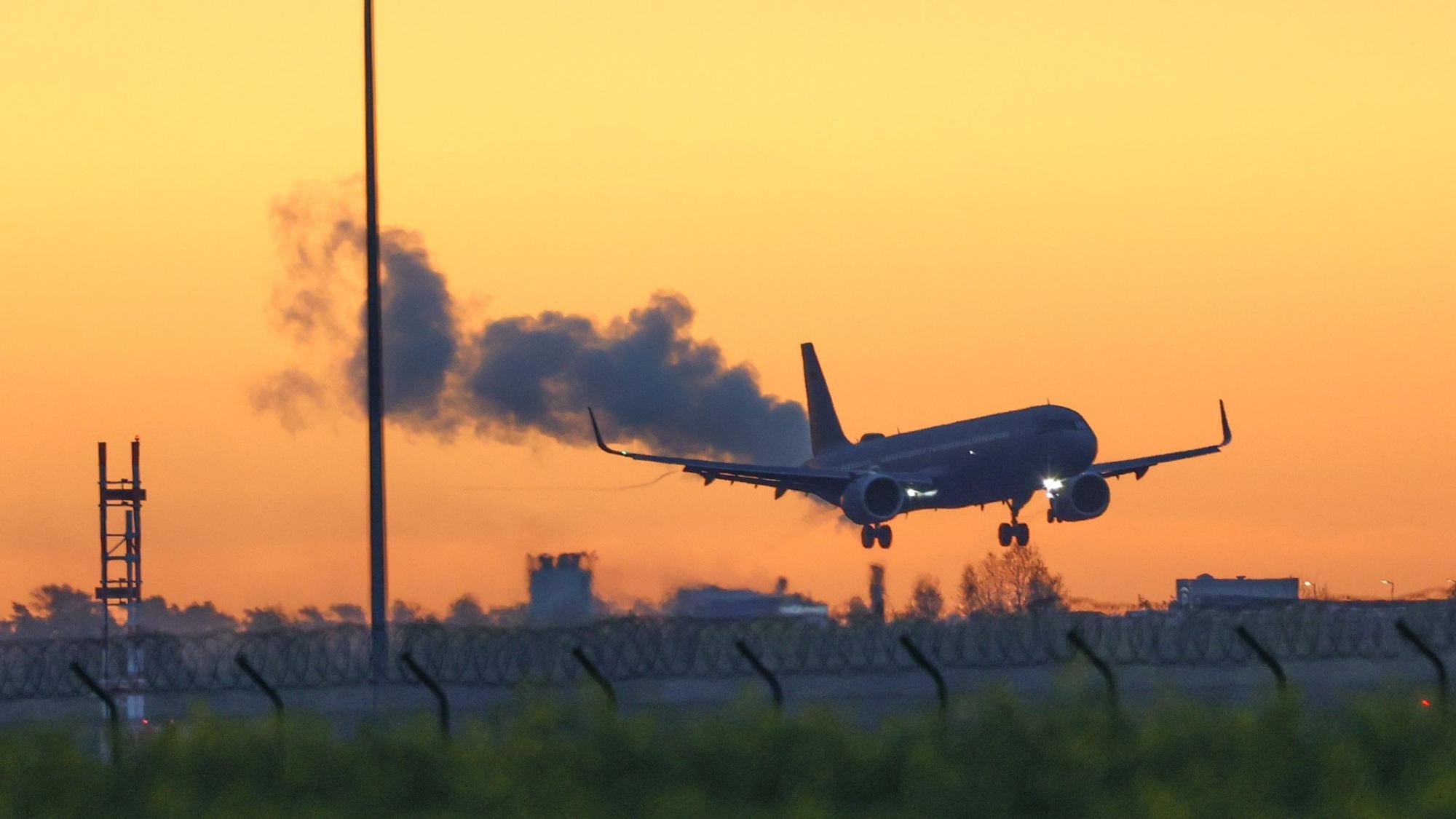 Ein Airbus der Luftwaffe fliegt vor einem goldenen Morgenhimmel den Flughafen BER in Berlin an.