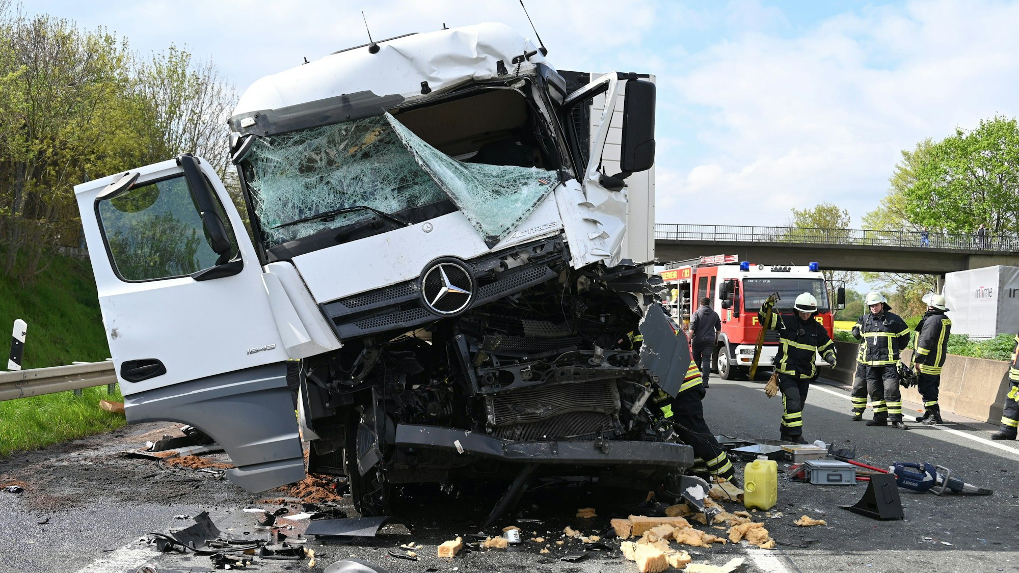 Ein Lkw mit einem total beschädigten Führerhaus steht auf einer Autobahn. Drumherum stehen Einsatzkräfte der Feuerwehr.