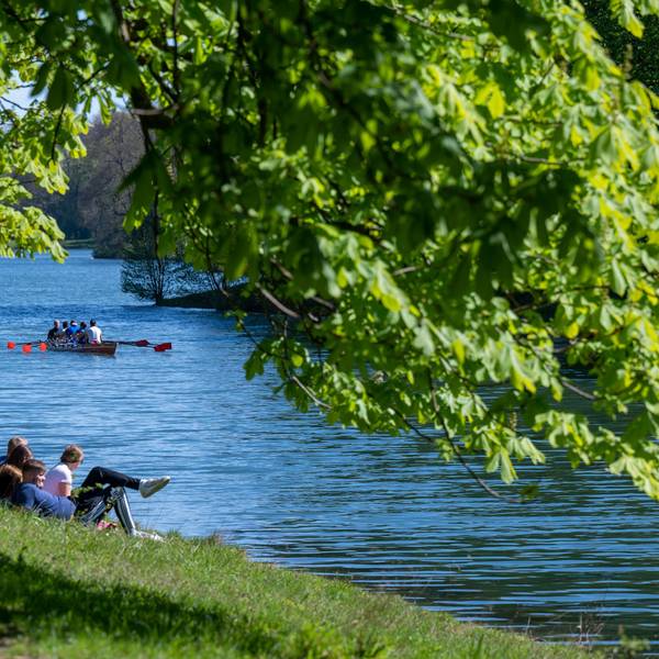 Der Decksteiner Weiher, einige Menschen entspannen am Wasser, ein Boot schippert den Kanal hinunter, es ist sonnig