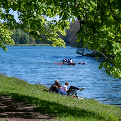 Der Decksteiner Weiher, einige Menschen entspannen am Wasser, ein Boot schippert den Kanal hinunter, es ist sonnig