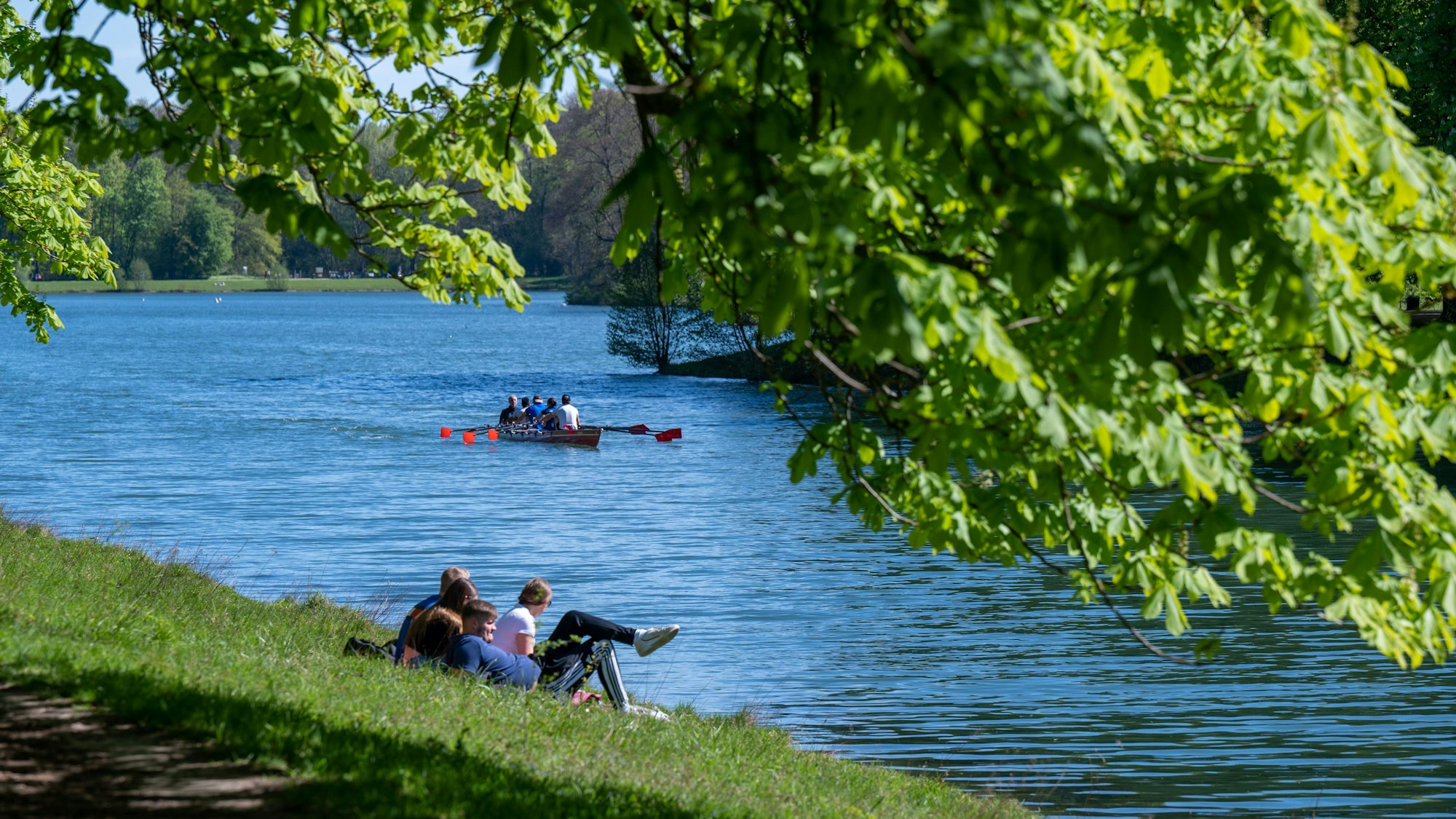 Der Decksteiner Weiher, einige Menschen entspannen am Wasser, ein Boot schippert den Kanal hinunter, es ist sonnig
