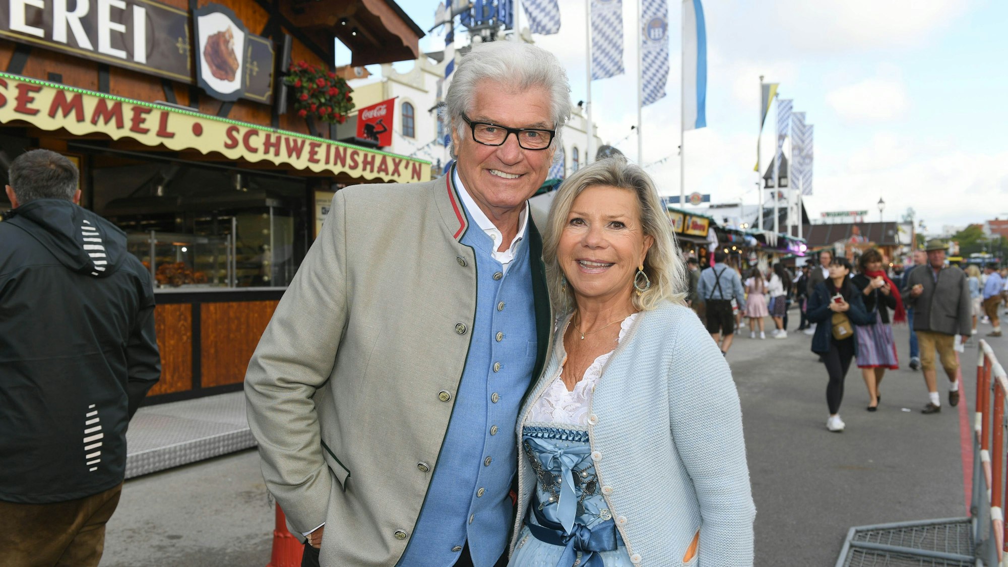 Marianne und Michael auf dem Münchner Oktoberfest 2022. Im Hintergrund sieht man Buden und Menschen in Tracht.