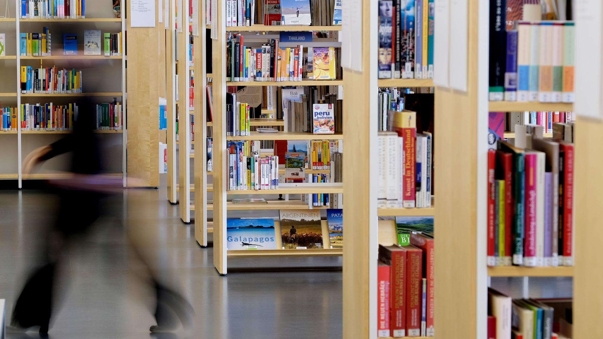 Eine Mitarbeiterin geht an Bücherregalen vorbei. (Symbolbild)