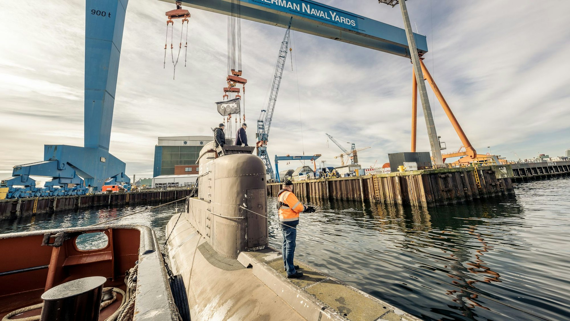 Ein großes U-Boot liegt im Wasser bei Kiel. Ein Mann in einer orangenen Jacke steht auf dem oberen Teil des Bootes.