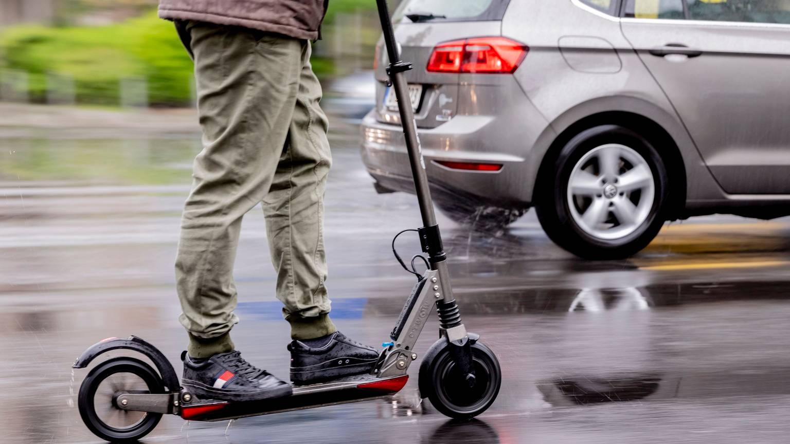 Ein Mensch steht auf einem E-Scooter, der auf einer nassen Straße fährt