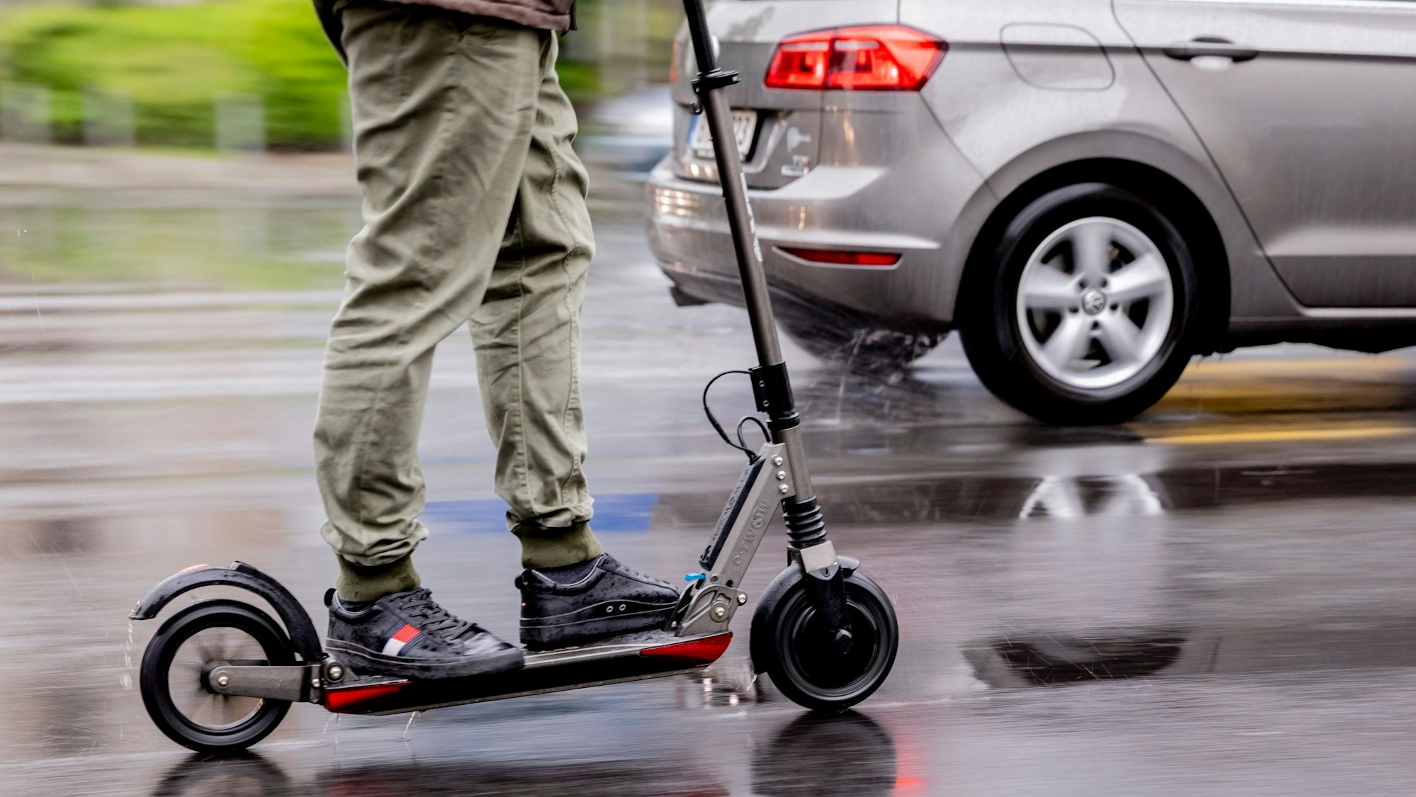 Ein Mensch steht auf einem E-Scooter, der auf einer nassen Straße fährt