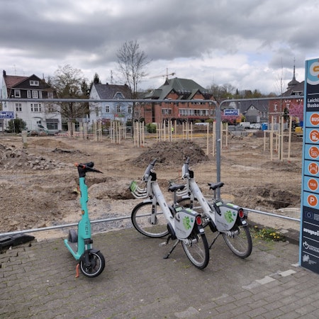 Zwei Leihräder und ein Roller stehen an der eingezäunten Mobilstation neben der Baustelle am Stadtpark Leichlingen